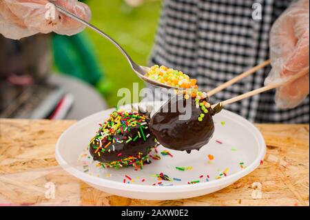 Gefrorene Erdbeeren in Schokolade auf einem Stock. Frau streut Dessert. Selektiver Fokus Stockfoto