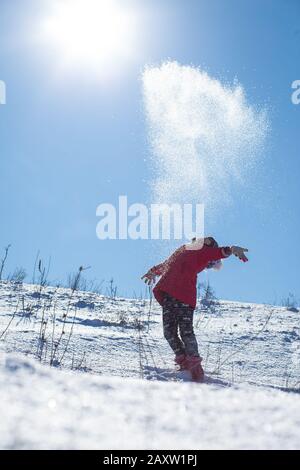 Kleines Mädchen wirft an einem frostigen klaren Tag Schnee in die Luft. Kinder genießen den Schnee. Stockfoto