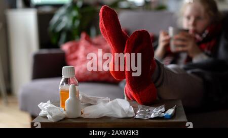 Porträt eines kranken Kindes in einem Schal und Plaid mit einer Tasse heißen Tee auf dem Sofa in der Wohnung, Drogen im Vordergrund Stockfoto