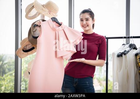 Schöne, glückliche Asianerin in rotem T-Shirt mit hellrosa Kleid im Bekleidungsgeschäft. Stockfoto