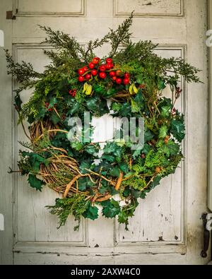 Handgefertigter Weihnachtskranz hängt an rustikaler Tür. Stockfoto