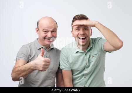 Aufgeregte kaukasische Männer Vater und Sohn sind überrascht, als sie mit dem Daumen auf die Kamera schauen, weißer Studiohintergrund Stockfoto
