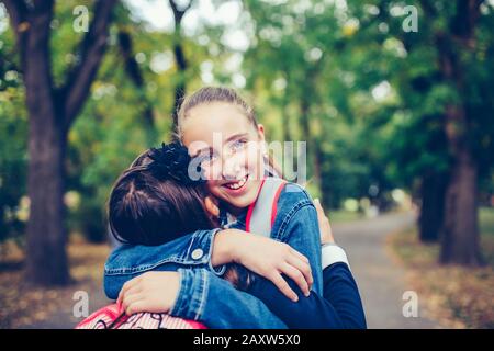 Zwei Schulfreunde umarmen, emotionales Treffen im Park. Das Konzept von Schule, Studium, Bildung, Freundschaft, Kindheit Stockfoto