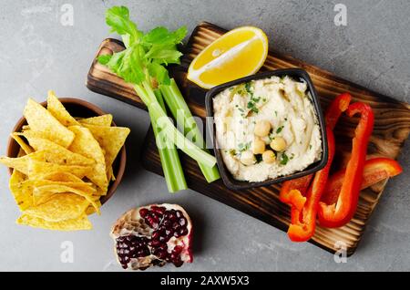 Flacher Laienblick auf die mit Kichererbsen und Olivenöl bestockte Gemüsesummus-Tauchform, serviert mit Tortilla-Pommes, Sellerie und Paprika Stockfoto