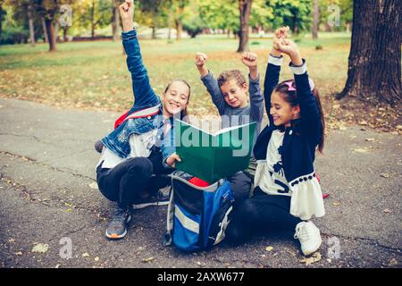 Glückliche kleine Kinder feiern Erfolg mit dem Anheben der Hände. Drei glückliche Kinder feiern ausgezeichnete Ergebnisse bei einem Test in der Schule. Stockfoto
