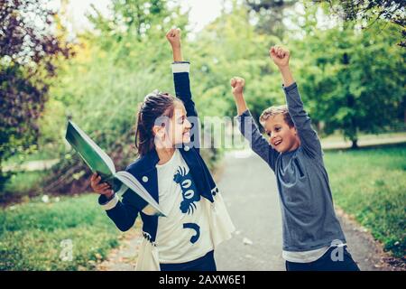 Glückliche kleine Kinder feiern Erfolg mit dem Anheben der Hände. Zwei glückliche Kinder feiern ausgezeichnete Ergebnisse bei einem Test in der Schule. Stockfoto