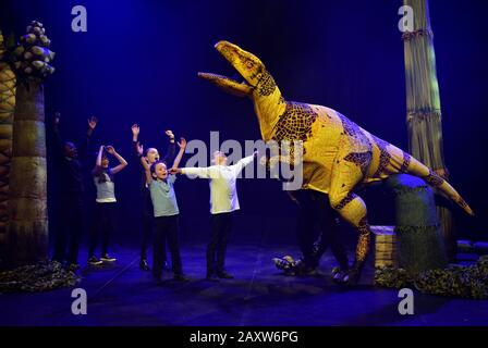 Kinder der Stockwell Primary School in London interagieren mit einer Fukuiraptor Dinosaurier-Marionette aus Erths Dinosaurier-Zoo in der Queen Elizabeth Hall im Southbank Center, London, vor einer Aufführung im Rahmen des Imagine Children's Festivals. Stockfoto