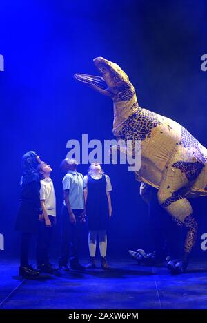 Kinder der Stockwell Primary School in London interagieren mit einer Fukuiraptor Dinosaurier-Marionette aus Erths Dinosaurier-Zoo in der Queen Elizabeth Hall im Southbank Center, London, vor einer Aufführung im Rahmen des Imagine Children's Festivals. Stockfoto