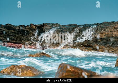 Wellen, die auf Felsen abstürzen, schließen sich unter der hellen Sonne Stockfoto