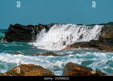 Wellen, die auf Felsen abstürzen, schließen sich unter der hellen Sonne Stockfoto