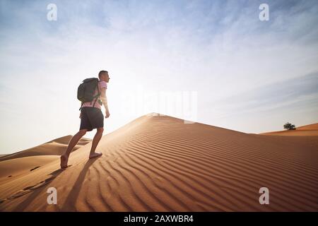 Abenteuer in der Wüste. Junger Mann mit Rucksack, der auf Sanddüne läuft. Abu Dhabi, Vereinigte Arabische Emirate Stockfoto
