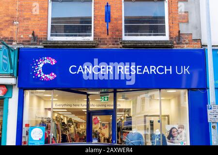 Charity-Zeichen von Cancer Research UK über dem Eingang zum Shop, in dem gespendete Gegenstände aus zweiter Hand verkauft werden Stockfoto