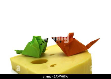 Origami-Maus mit orangefarbenem und grünem Papier in der Nähe einer großen Käsescheibe, die auf wihitem Hintergrund isoliert ist. Kopierbereich. Stockfoto