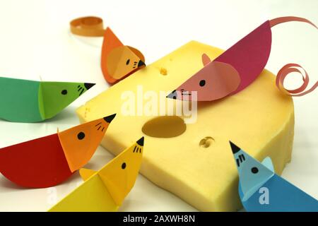 Bunte Origami-Mäuse mit lockem Schwanz auf einer großen Scheibe Käse isoliert auf wihitem Hintergrund. Kopierbereich. Stockfoto