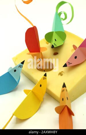 Bunte Origami-Mäuse mit lockem Schwanz auf einer großen Scheibe Käse isoliert auf wihitem Hintergrund. Kopierbereich. Stockfoto