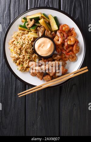 Hibachi-Gericht, bestehend aus gebratenem Reis mit Ei, Garnelen, Steak und Gemüse, serviert mit Sauce in einem Teller auf dem Tisch. Vertikale Draufsicht von Stockfoto