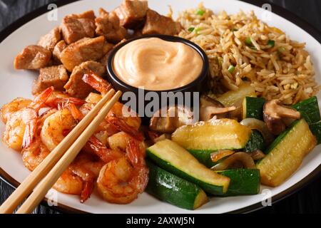 Hibachi Gericht bestehend aus gebratenem Reis mit Ei, Garnelen, Steak und Gemüse, serviert mit Sauce in einem Teller auf dem Tisch. Horizontal Stockfoto