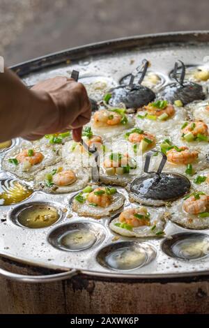 Straßennahrungsmittel, die vietnamesische Mini-Garnelen-Pfannkuchen machen - Banh Khot Stockfoto