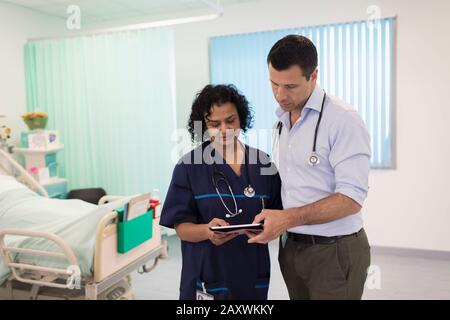 Ärzte mit digitaler Tablette runden ab und beraten im Krankenhauszimmer Stockfoto