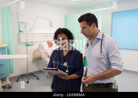 Ärzte mit digitaler Tablette runden ab und beraten im Krankenhauszimmer Stockfoto