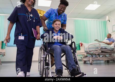 Arzt und Krankenschwester schieben den Jungen im Rollstuhl in der Krankenstation Stockfoto