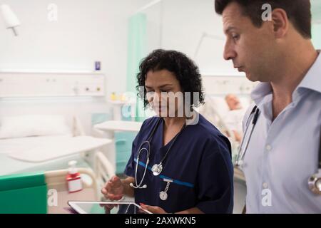 Ärzte mit digitaler Tablette runden ab und beraten im Krankenhauszimmer Stockfoto