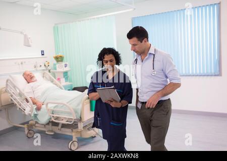 Ärzte mit digitaler Tablette runden ab und beraten im Krankenhauszimmer Stockfoto