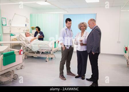 Ärzte mit digitaler Tablette runden ab und beraten im Krankenhauszimmer Stockfoto