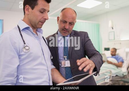 Männliche Ärzte mit digitaler Tablette runden ab und beraten im Krankenhauszimmer Stockfoto