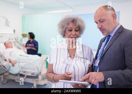 Ärzte mit digitaler Tablette runden ab und beraten im Krankenhauszimmer Stockfoto
