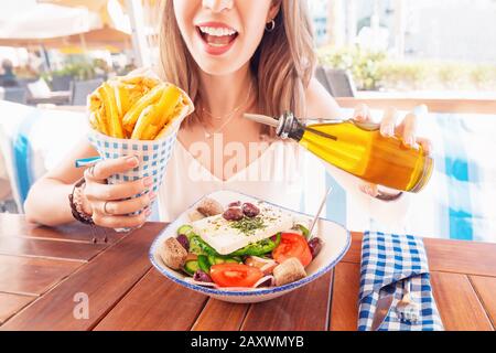 Fröhliches Touristenmädchen probiert griechische Küche in einem lokalen Restaurant. Auf dem Tisch traditionelle Salate Horiatiki und Gyros in Pita Stockfoto