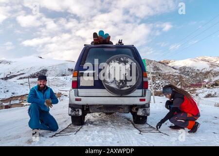 Jungs haben sich auf eine Autoreifenkette gesetzt, um auf rutschigen Straßen zu fahren. Wintersaison. Stockfoto