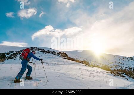 Ein Mann ist mit dem Skituring auf geteiltem Snowboarding beschäftigt. Sonnenaufgang ist in den Bergen sonnig. Kirgisistan Stockfoto