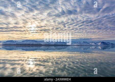 Schneebedeckte Berge am Billefjorden bei Sonnenuntergang und Wolken, die sich im arktischen Meer, im zentralen Fjord des Isfjordes, Svalbard/Spitzbergen, Norwegen widerspiegeln Stockfoto