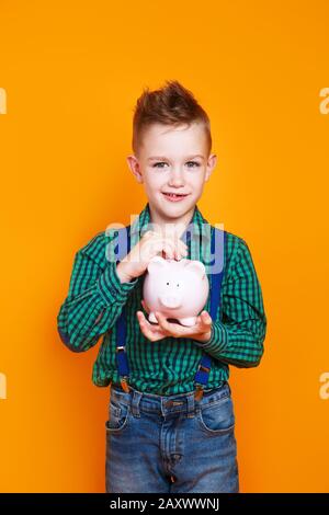 Kleiner Junge mit einer Schweinebank auf gelbem Hintergrund. Finanzkonzept Kindertaschengeld. Stockfoto