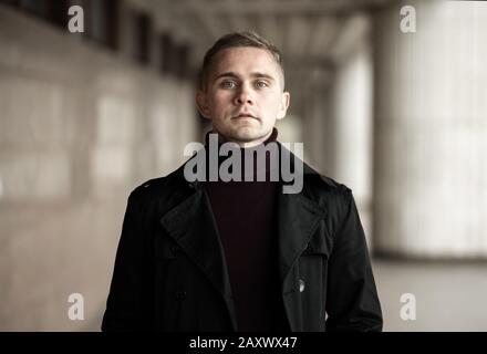 Stilvoller Mann mit schwarzem Trenchcoat und violettem Polokragen Stockfoto