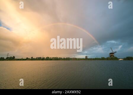 Heller Regenbogen über einem See mit Windmühle, die am Ufer steht Stockfoto