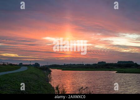 Sonnensäule in bunten Wolken kurz nach Sonnenuntergang. Atmosphärisches optisches Phänomen. Stockfoto