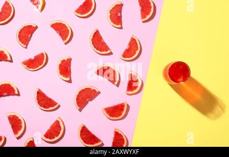 Frische Grapefruitscheiben auf pinkfarbenem Hintergrund und kalte Grapefruitgetränke auf gelbem Hintergrund in der Sommersonne. Bicolor Hintergrund und saftige Grapefruit. Stockfoto