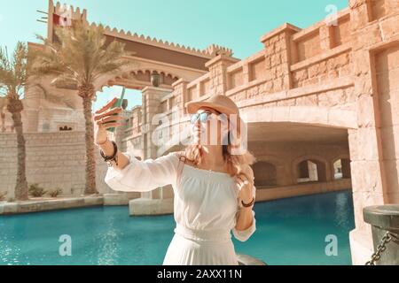 Fröhliches asiatisches Mädchen in weißem Kleid mit selfie-foto auf ihrem Smartphone vor dem Hintergrund der mittleren östlichen Altstadt. Reisen und Urlaub in Dubai und Stockfoto