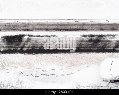 Über dem Blick auf die Fußabdrücke auf der schneebedeckten Straßendecke der gerodeten Stadtstraße im Winter Stockfoto