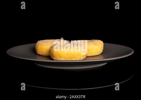 Gruppe von drei ganzen süßen goldenen Mini-Zimt-Donut auf grauer Keramikplatte isoliert auf schwarzem Glas Stockfoto