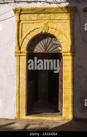 Gelbe Türfassade mit traditionellen Details. Leuchtend gelbe Farbe, die von der Sonne erhellt wird. Tür geöffnet. Essaouira, Marokko. Stockfoto