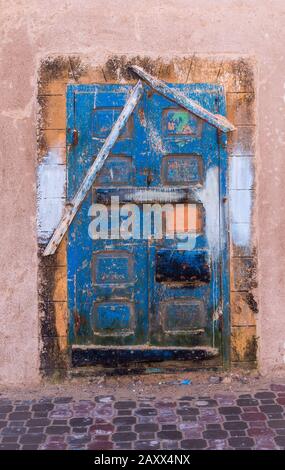 Meist blau lackierte Holztür, mit Details anderer Farben. Sehr alt und verwittert, genauso wie die Fassade des Hauses. Essaouira, Marokko. Stockfoto