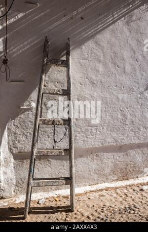 Weiß strukturierte verwitterte Wand mit einer stehenden alten Leiter aus Holz. Straße von Essaouira, Marokko. Stockfoto