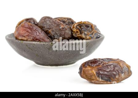 Gruppe von sechs ganzen trockenen braunen Datumsfrüchten in dunkler Keramikschale isoliert auf weißem Grund Stockfoto