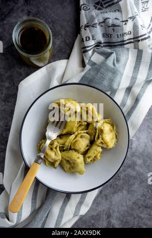 Gekochte Tortellini auf einem Teller, Nudeln aus der Nähe, italienische Küche. Dunkler Hintergrund. Stockfoto