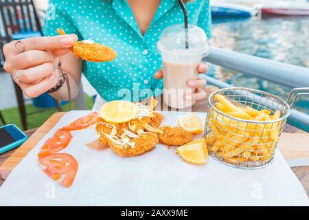 Ein Mädchen isst Garnelen in Teig und Pommes frites auf der Terrasse eines Meercafés Stockfoto