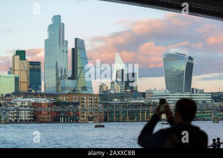 London, Großbritannien. Februar 2020. Sonnenuntergang, eine Person unter der Blackfriars Bridge macht ein Bild von Wolken, die den Sonnenuntergang über der City of London Skyline während der Flut im Frühjahr widerspiegeln. Kredit: Thamesfleet/Alamy Live News Stockfoto