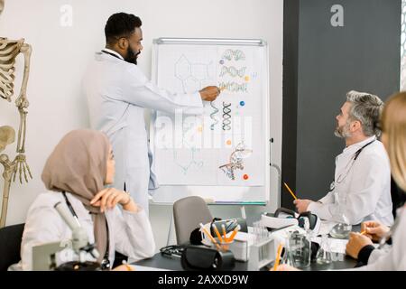 Interracial Gruppe von Ärzten, Chemikern und Wissenschaftlern, die sich bei einem Treffen mit dem jungen Afrikaner treffen, der neue Informationen erzählt und zeigt Stockfoto